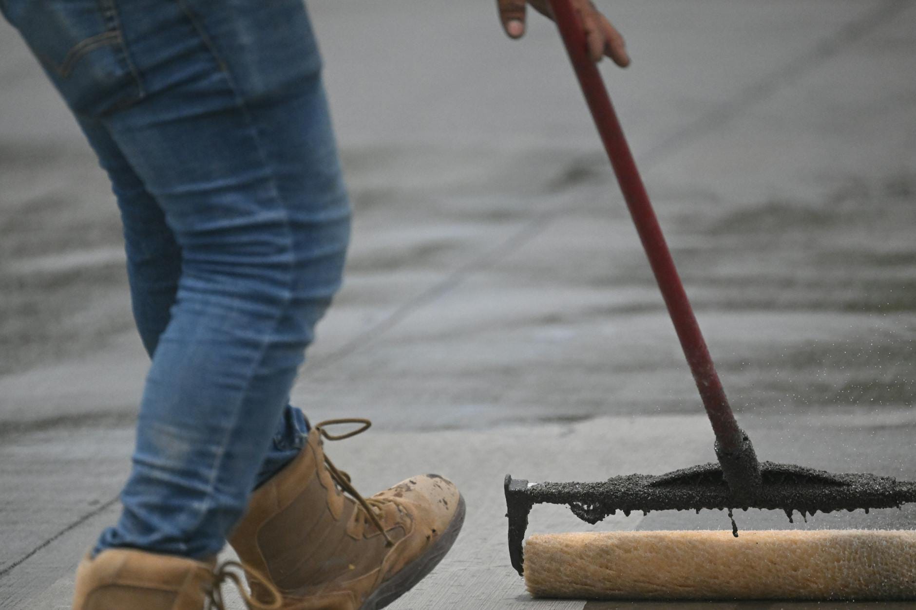 Nakładanie impregnatu wałkiem na betonowy podjazd przez osobę w jeansach